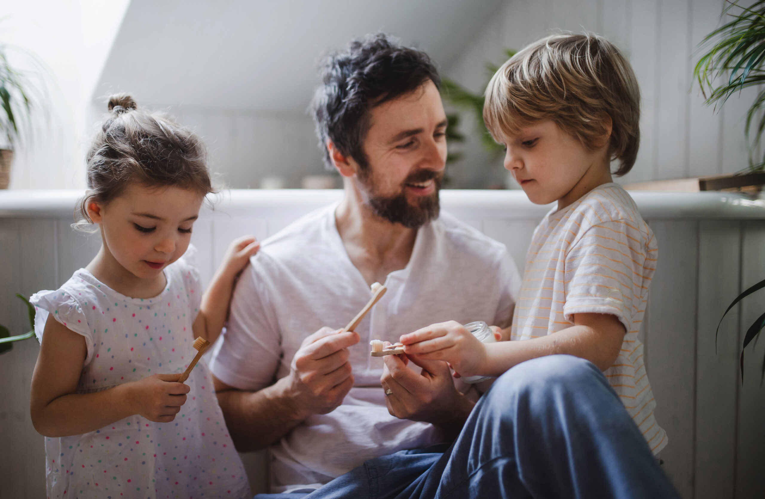Father teaching young children how to brush their teeth, promoting dental hygiene at home.