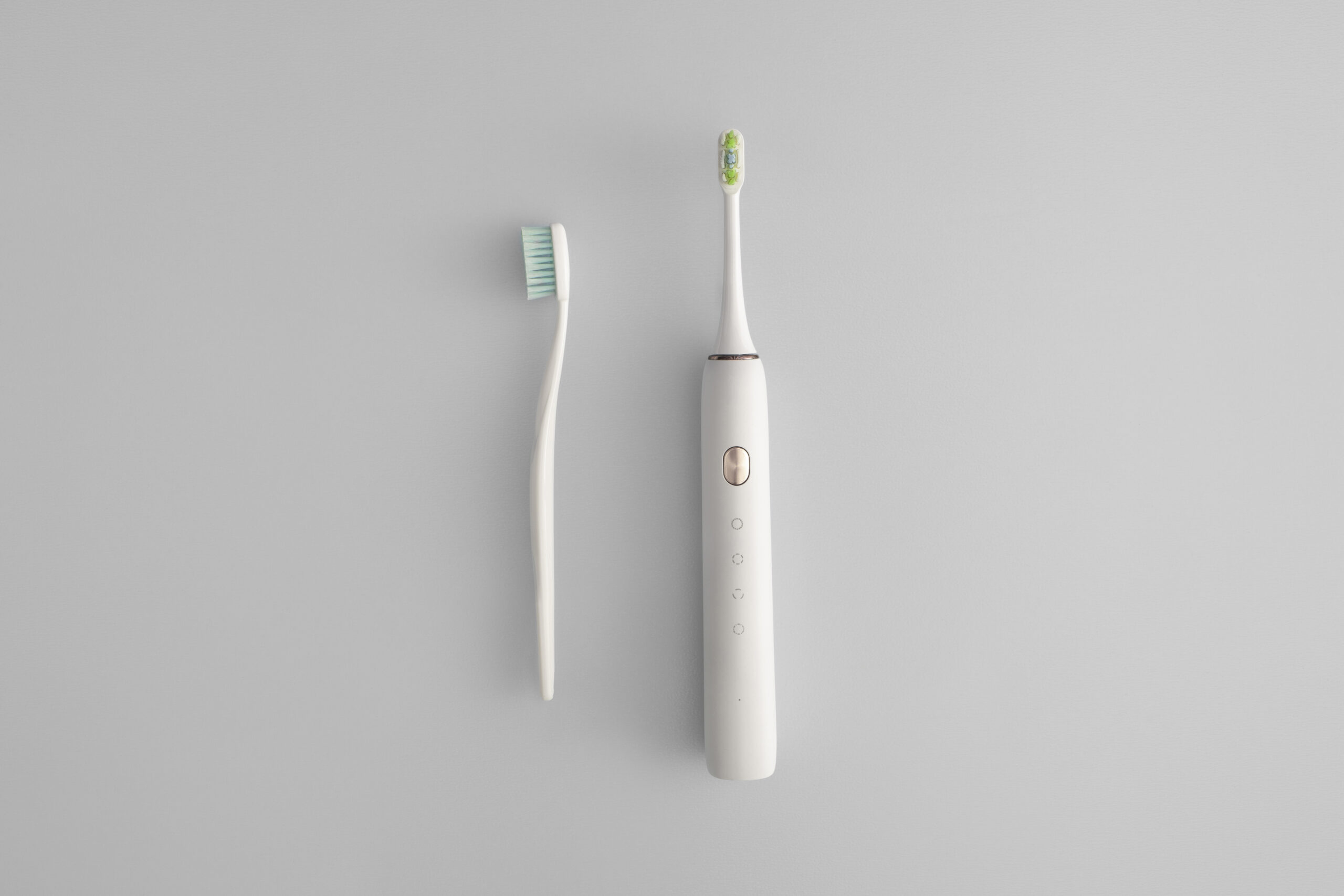 Side-by-side comparison of a manual toothbrush and an electric toothbrush on a gray background.