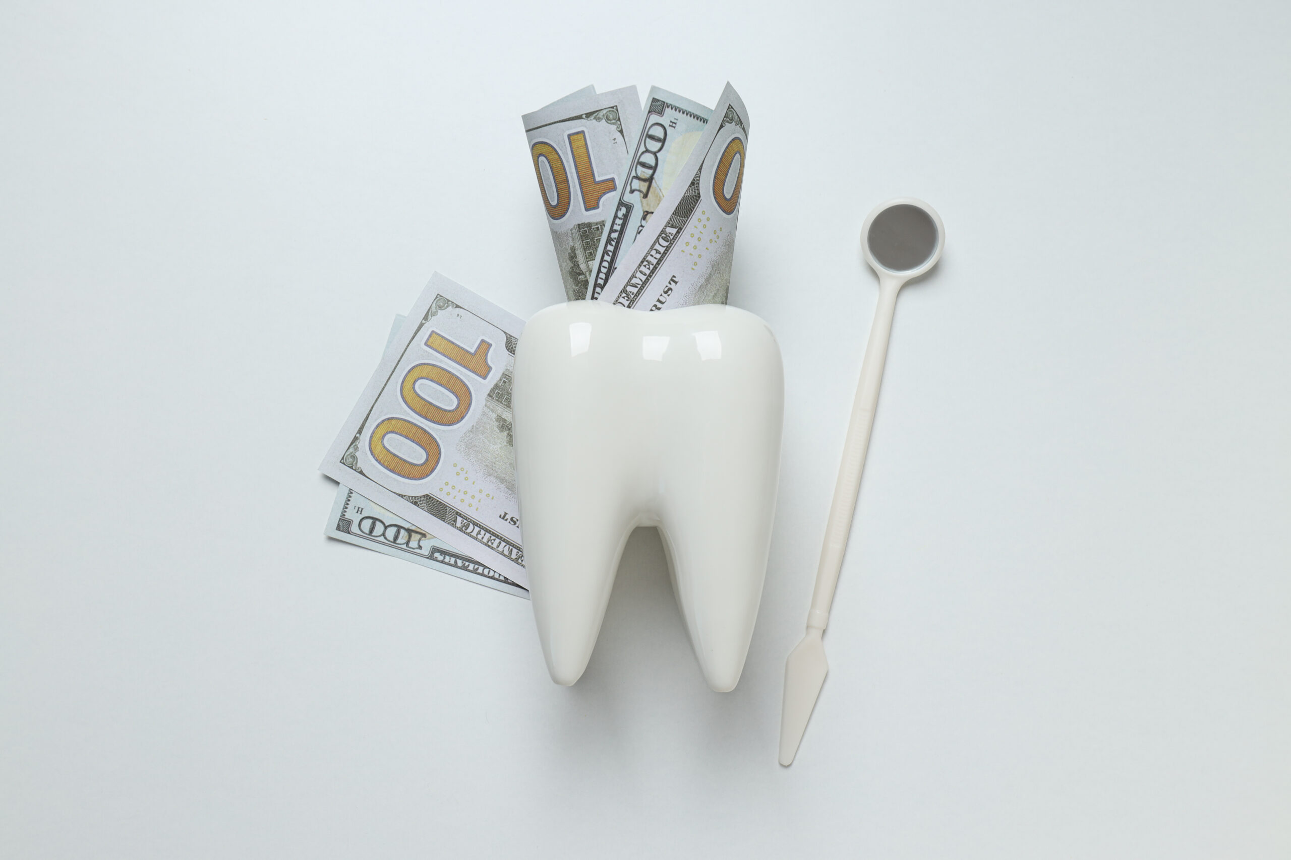A white tooth model with dollar bills inserted, symbolizing the cost of dental care in the U.S.