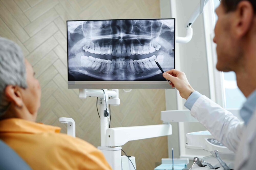 Dentist reviewing X-rays with a patient while discussing medication history and bone health