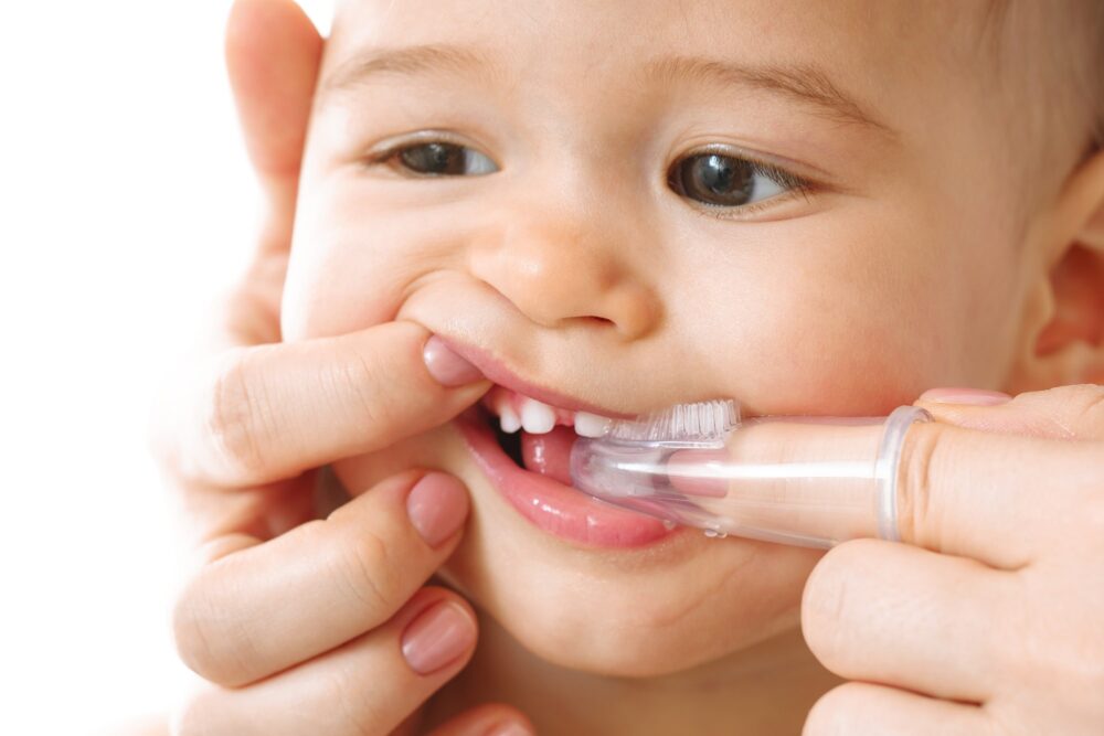 Parent using a finger brush to gently clean their baby’s first teeth