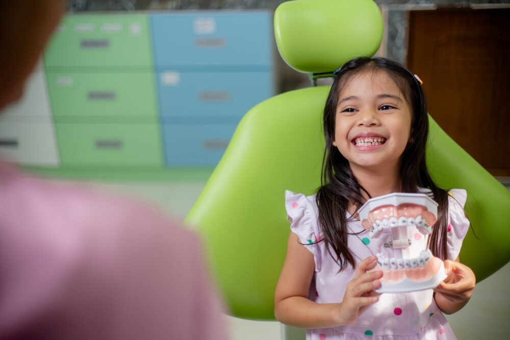 Smiling child holding a dental model while sitting in a dental chair during a pediatric checkup