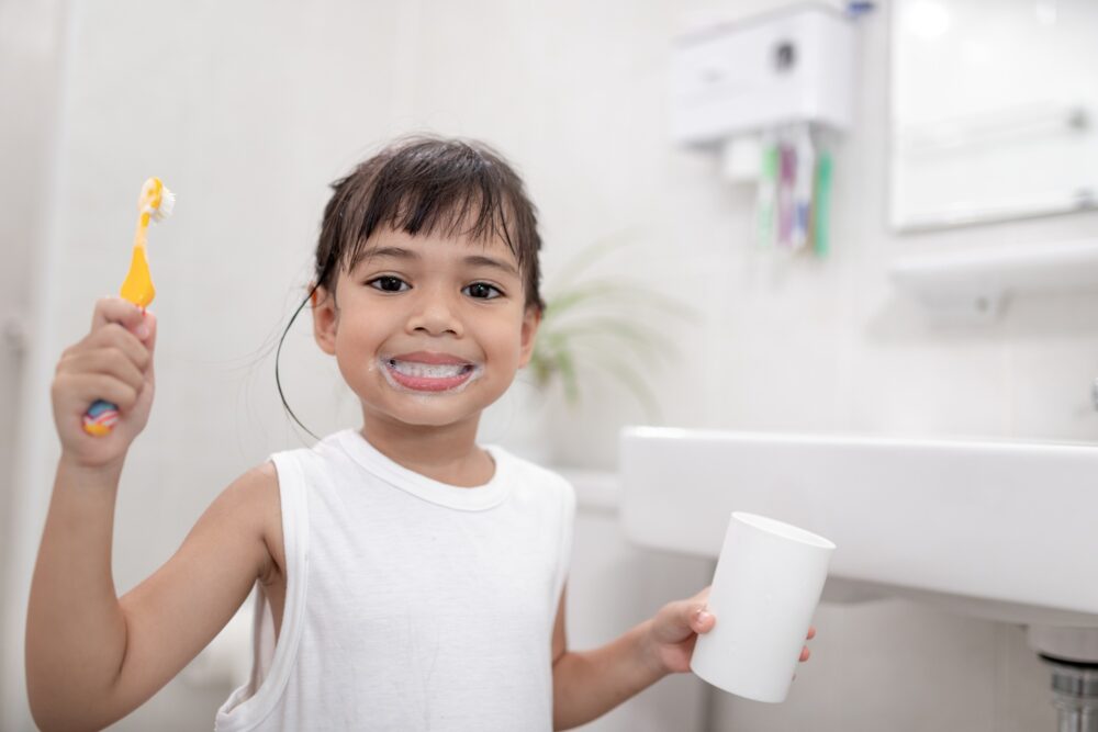 Smiling child brushing teeth with fluoride toothpaste in a bathroom