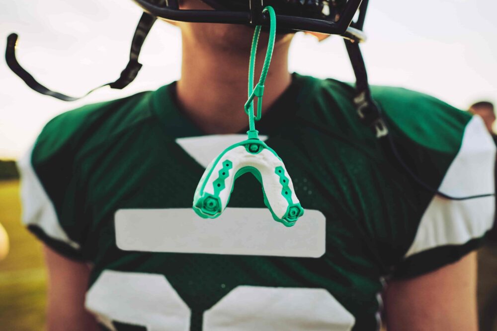 Close-up of a green and white football mouthguard hanging from a player’s helmet during a game