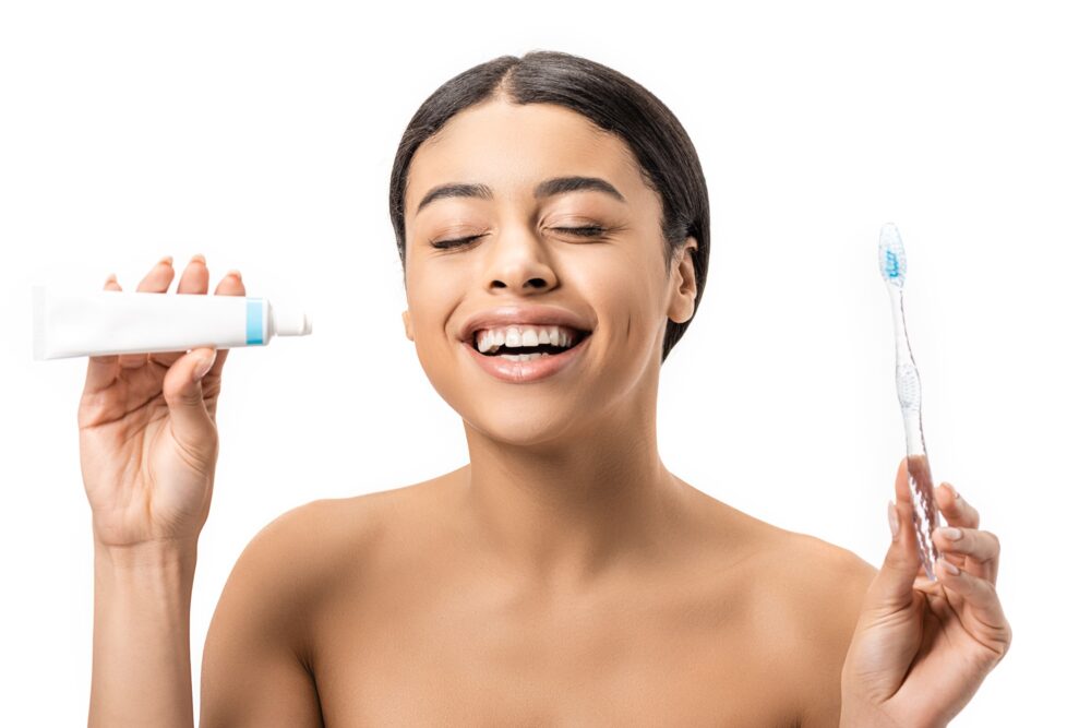 Smiling woman holding toothpaste and toothbrush, representing daily teeth whitening routine