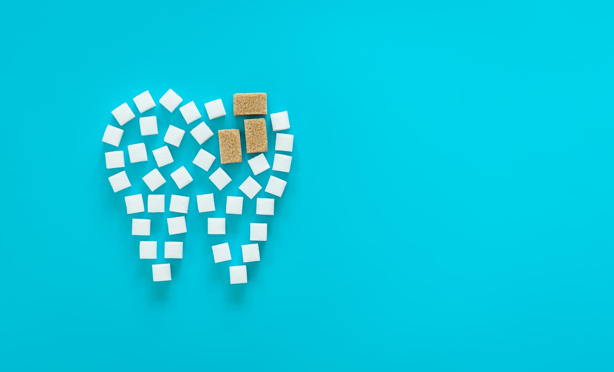 White sugar cubes arranged in the shape of a tooth on a blue background, symbolizing the effect of sugar on dental health
