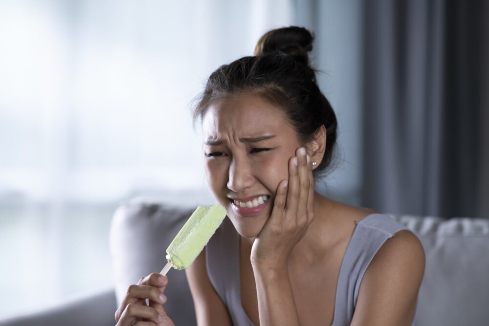 Woman experiencing tooth pain while eating ice cream due to sensitivity