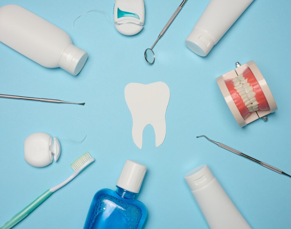 Flat lay of toothbrush, floss, mouthwash, and dental tools around a tooth illustration on blue background