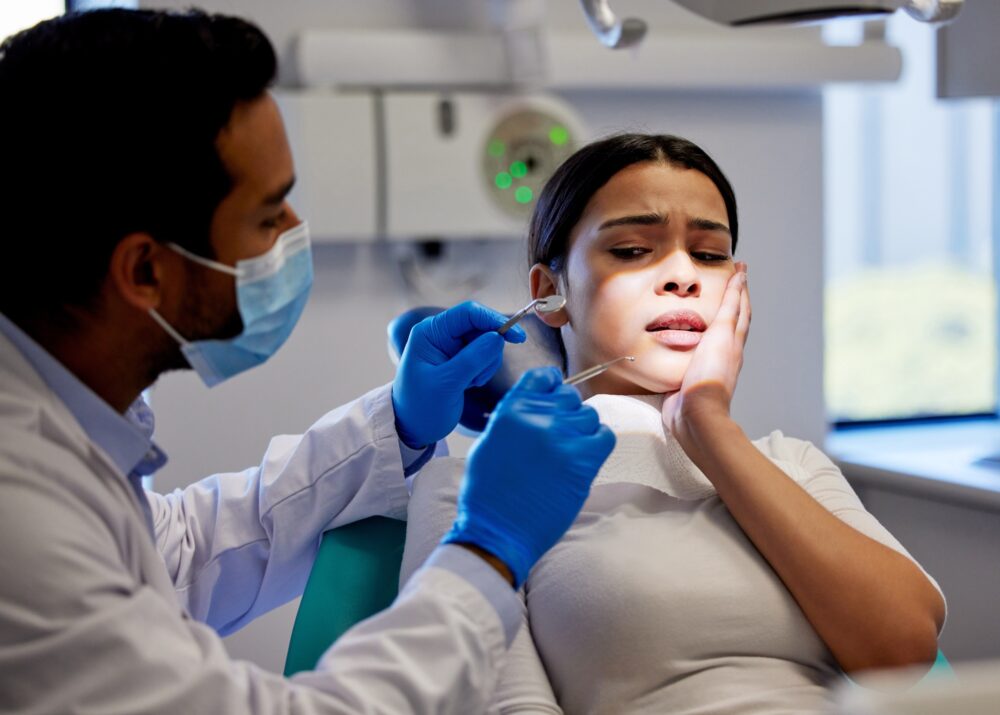 Female dental patient holding her cheek in pain while being examined by a dentist in an emergency appointment