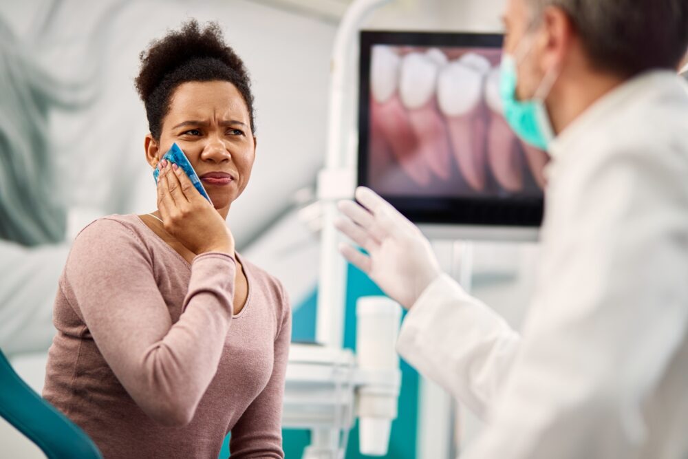 Woman holding an ice pack to her cheek while consulting a dentist about dental pain or trauma