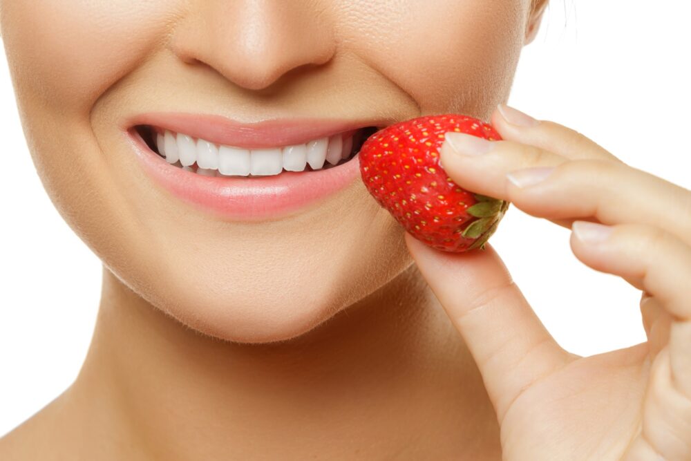 Woman smiling while holding a strawberry near her teeth